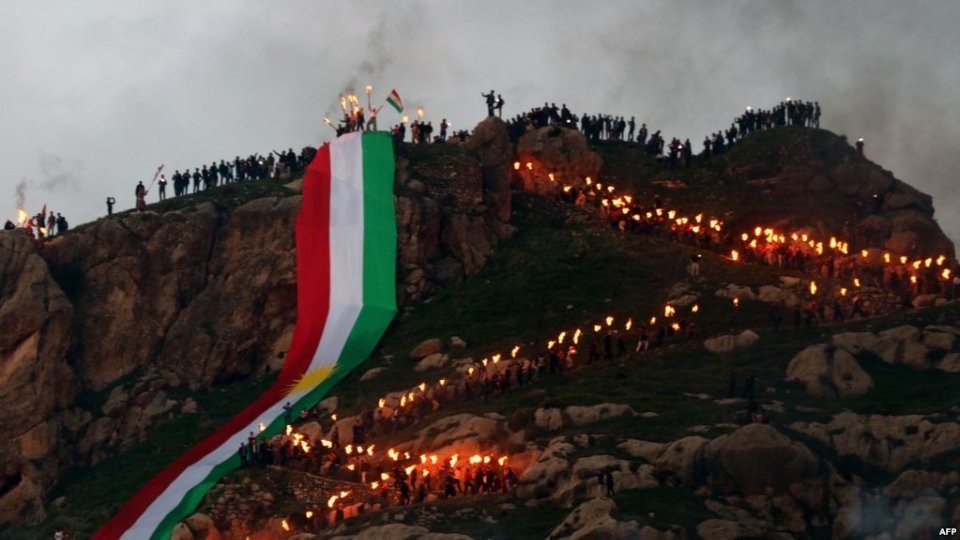 إشعال نار النوروز على جبال كُردستان، بينما يتدلى منها علم كُردي كبير