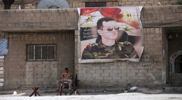 صورة بشار الأسد معلقة على بيت وبجانبها عسكري(انترنت)